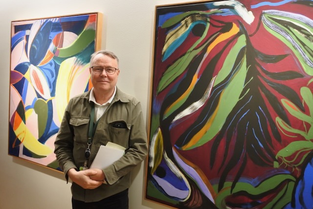 BRÅDA DAGAR. Martin Joanson framför Malin Gabriella Nordins färgglada tavlor, har fullt upp. Varje år lotsar han runt mer än 100 besöksgrupper.